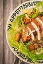 Caesar salad with thinly sliced chicken breast and traditional aioli on a plate that says bon apetite on a rustic table. Top view Royalty Free Stock Photo