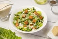 Caesar salad in a white bowl with leaves and a sauce boat and parmesan. Selected focus.