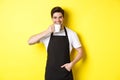 Cafe barista drinking cup of coffee and smiling, wearing black apron, standing over yellow background Royalty Free Stock Photo