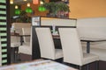 Cafe interior fragment, view on white chairs and table on the background of orange wall. Cafe is decorated with multicolored lamps