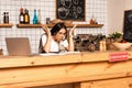 Cafe owner looking at calculator near papers and laptop at table with card with coronavirus inscription