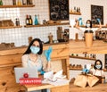 Cafe owner showing okay sign, paper bags near tables with disposable cup of coffee, papers, laptop and card with