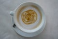 Caffe latte with latte art in rose flower pattern on milky foam layer in white cup and saucer on white textured table cloth