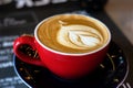 Caffee latte macchiato cappuccino in red mug in cafe house with milk foam art