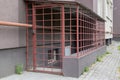 Cage with locked gate of red metal with black padlock, enclosing entrance to basement with white door and gas pipe passing over it