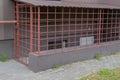 Cage with locked gate of red metal with black padlock, enclosing entrance to basement with white door and gas pipe passing over it