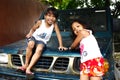Young Filipino children play on a parked vehicle and smile for the camera