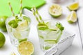Caipirinha, mojito cocktail with lime, brown sugar, ice and mint leaves in beautiful glasses, cut green citrus on white wooden bac Royalty Free Stock Photo