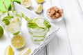 Caipirinha, mojito cocktail with lime, brown sugar, ice and mint leaves in beautiful glasses, cut green citrus on white wooden bac Royalty Free Stock Photo