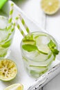 Caipirinha, mojito cocktail with lime, brown sugar, ice and mint leaves in beautiful glasses, cut green citrus on white wooden bac Royalty Free Stock Photo