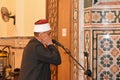 A mosque Imam preacher muezzin in front of the microphone reciting Adhan Azan or calling loudly for the prayer