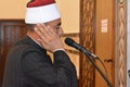 A mosque Imam preacher muezzin in front of the microphone reciting Adhan Azan or calling loudly for the prayer