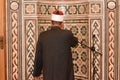 A mosque Imam preacher muezzin in front of the microphone reciting Adhan Azan or calling loudly for the prayer