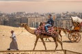 CAIRO, EGYPT - MAY 18 2021: Bedouin camel driver rides an Asian tourist from China on a camel, on the Giza plateau. Asian tourist