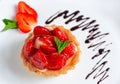 appetizing strawberry tartlet glazed with clear jelly, on a white plate with chocolate icing Royalty Free Stock Photo