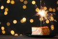 Cake with burning sparkler on black table against blurred festive lights. Space for text Royalty Free Stock Photo