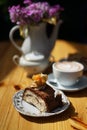 Cake with chocolate on a plate next to a cup of coffee, a sugar bowl and a vase of flowers on a wooden table Royalty Free Stock Photo