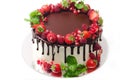 Cake covered with berries of raspberry strawberry pomegranate mint leaves doused with chocolate on an isolated white background.