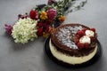 Cake covered with chocolate decorated raspberries, with a bouquet of flowers on a gray background.