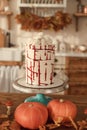 The cake is decorated with skulls and blood for Halloween. Kitchen is decorated for autumn