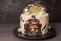 Cake with the image of Batman, decorated with lollipops, chocolate balls, bats. Birthday cake with a comic book hero