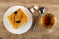 Cake with jam and prune in plate, sugar cubes, spoon, cup with tea on wooden table. Top view Royalty Free Stock Photo