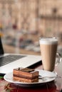 Girl eating piece of cake and cup of latte coffee in a cafe on the blur background of city Royalty Free Stock Photo