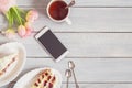 Cake, phone, cup of tea and pink tulips on white wooden table