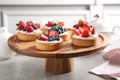 Cake stand with different berry tarts on table