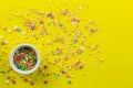 Cake topping prinkles on bright yellow background with little white bowl with various type of coloured sprinkles at bottom and