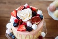 Cake with various berries, figs, meringues and rose on top.