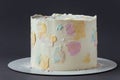 Cake with white cream cheese frosting decorated with multicolored smears on the dark grey background. Blank cake with a free space