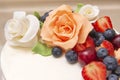 Cake with white mastic decorated with beige roses from mastic and fresh berries, strawberries, cherries, blueberries