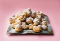 Cakes profiteroles sprinkled with powdered sugar on a pink background. Homemade eclairs.