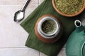 Calabash, bombilla, bowl of mate tea leaves and teapot on tiled table, flat lay