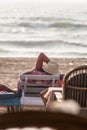 Back shot of a female Caucasian tourist wearing a hat lying on a beach bed by the sea and