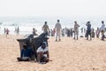 Two Indian men sitting beside trash cans on a crowded tourist beach in Goa