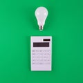 Calculation of electricity costs. Calculator and energy-saving light bulb on a green background. Top view. flat lay Royalty Free Stock Photo