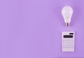 Calculation of electricity costs. Calculator and energy-saving light bulb on a purple background. Top view. flat lay Royalty Free Stock Photo