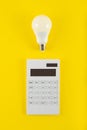 Calculation of electricity costs. Calculator and energy-saving light bulb on a yellow background. Top view. flat lay Royalty Free Stock Photo