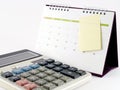 white calculator and desk calendar with blank yellow paper sticky note taped on calendar page