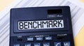 A calculator labeled BENCHMARK is on the table near the report. Financial concept