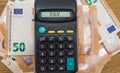 The calculator lies on a heap with 50 euros. Close-up. Business concept. The word tax on a calculator scoreboard.