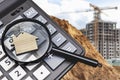 A calculator with a magnifying glass and a keychain in the shape of a house on the background of a construction site. Real estate