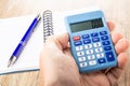 Calculator in male hand, ballpoint on open notepad on table