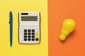 A calculator with a pen and a light bulb on an orange and yellow background Royalty Free Stock Photo