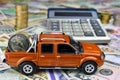 Calculator and pickup toy car with coins in the cargo box on a variety of national currency banknotes background.  Concept of the Royalty Free Stock Photo