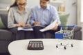 Calculator and shopping trolley up close, couple calculating expenses in background Royalty Free Stock Photo