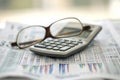 A calculator sits atop a pile of newspapers, creating an image of financial calculations and news analysis, Calculator and glasses