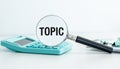 A calculator sits on a table with a magnifying glass over the word TOPIC. Royalty Free Stock Photo